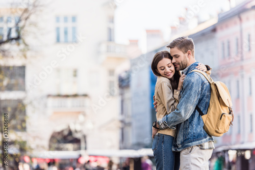 Boyfriend and girlfriend hugging with closed eyes and smiling in city