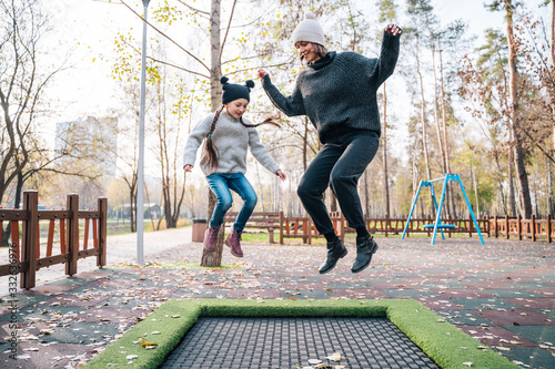 Mom and her daughter jumping together on trampoline in autumn park photo