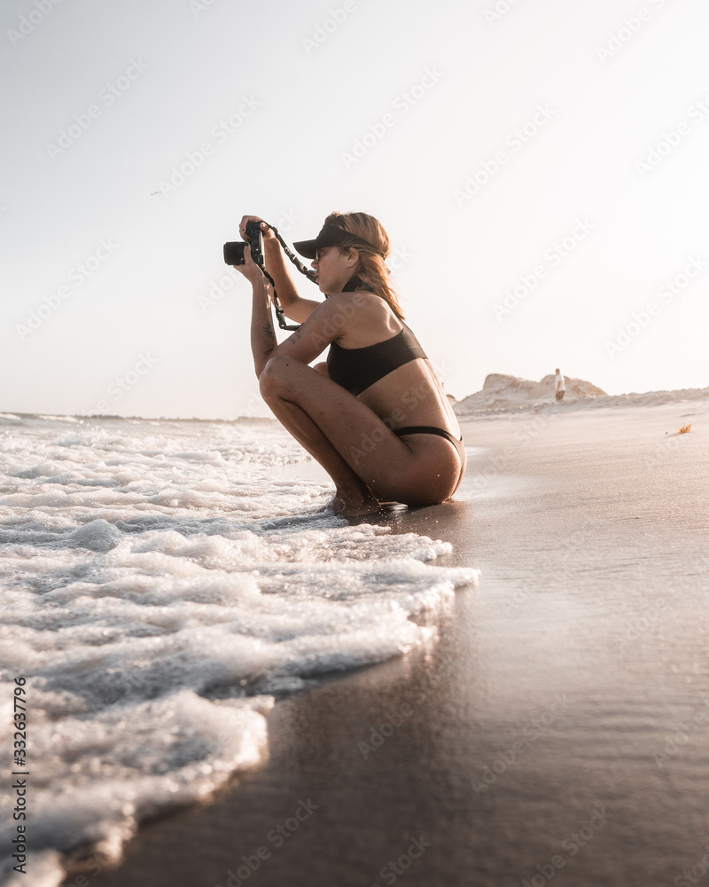 Chica agachada en la orilla haciendo foto al mar