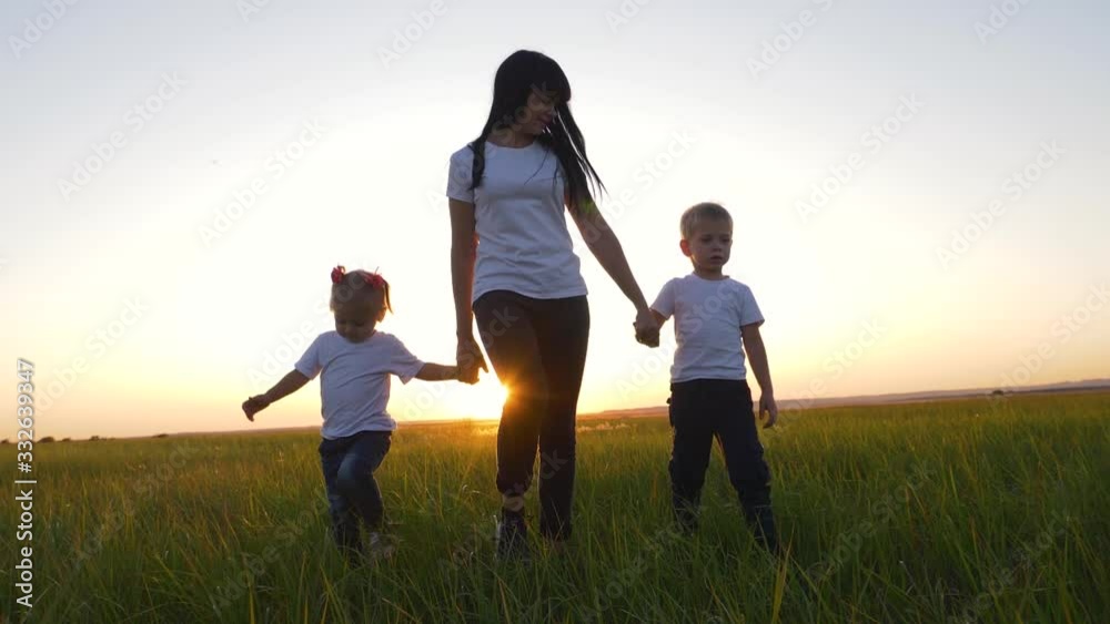 A young woman mother walks with two young children on the grass in the Park. A happy family walks outdoors in the setting sun. A young woman mother walks with two young children on the grass in the Park. A happy family walks outdoors in the setting sun.