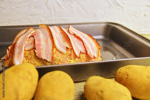 Meat loaf with slices of bacon. Home-made meat loaf on roasting pan. Potatoes foregraund. photo