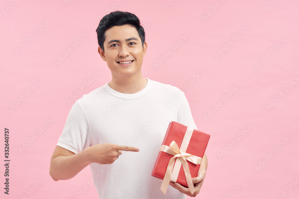 Handsome young man smiling and giving a red gift box to you isolated on pink background Handsome young man smiling and giving a red gift box to you isolated on pink background