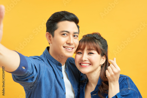 Self portrait of funny foolish cheerful adorable young cute couple smiling showing teeth, looking straight with opened mouths over yellow background, isolated