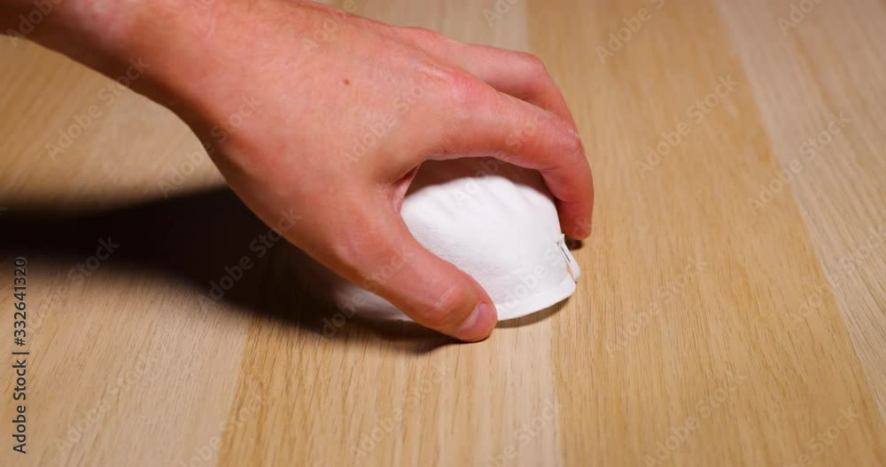 Men's hands lifting white protective mask on face and nose from wooden table on which lies protection against inhalation of corona covid virus Covid-19 capture in 4k 60fps