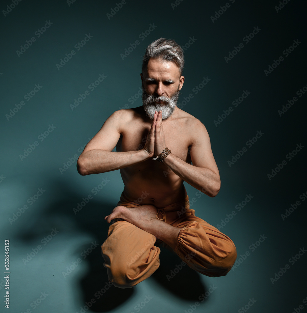 Obraz premium Old man with grey beard doing yoga, pilates, fitness training, stretching exercise, asana levitates or balance workout on floor