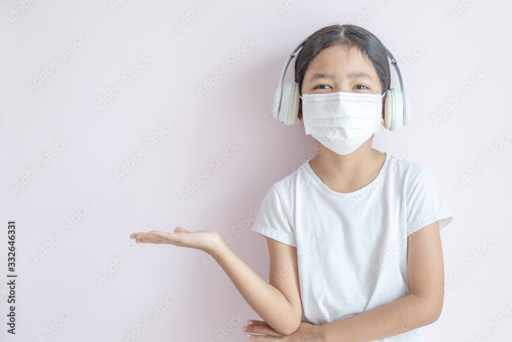 The little Asian girl wearing a medical protective mask and a headphone. The little Asian girl wearing a medical protective mask and a headphone.