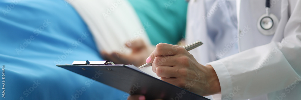 Focus on female tender hand holding pen and writing something in important documents. Beautiful doctor visiting ill patient. Healthcare and medicine concept