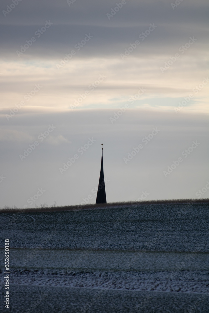 Fototapeta premium the roof of a church behind a hill at dusk