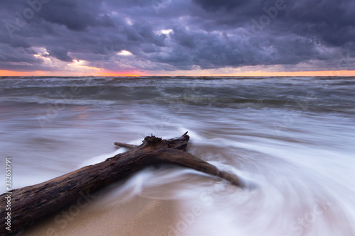 Dramatic shot of a tree log on a beach of Baltic Sea Coast during the storm weather. Long exposure 