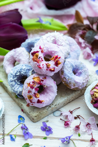 Table top scene of colorful doughnut cookies with edible flowers and birch sugar. Donut cookies. Pink and blue round raw cookies. Raw food, vegan menu. Black tulips.