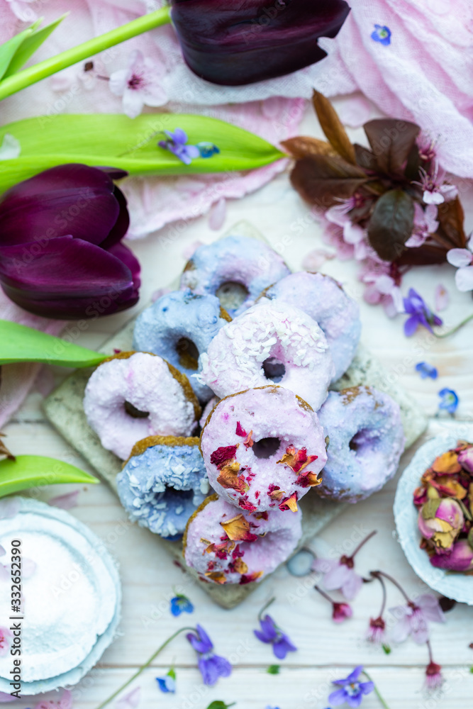 Table top scene of colorful doughnut cookies with edible flowers and birch sugar. Donut cookies. Pink and blue round raw cookies. Raw food, vegan menu. Black tulips. Table top scene of colorful doughnut cookies with edible flowers and birch sugar. Donut cookies. Pink and blue round raw cookies. Raw food, vegan menu. Black tulips.