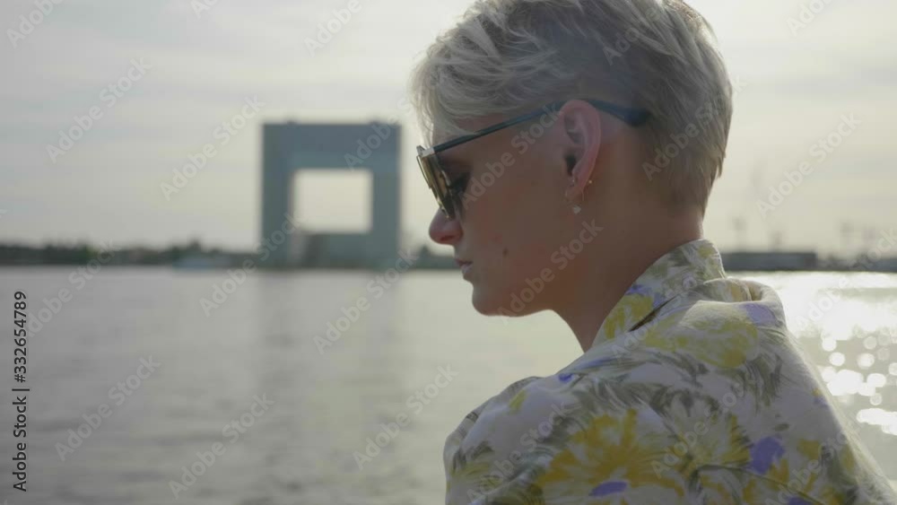 Young introspective woman sits on the pier next to the water. Close up profile shot.