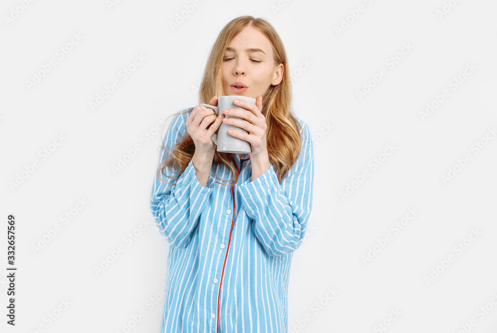 Beautiful girl in striped pajamas, with a Cup in her hands , drinking coffee or tea in the early morning
