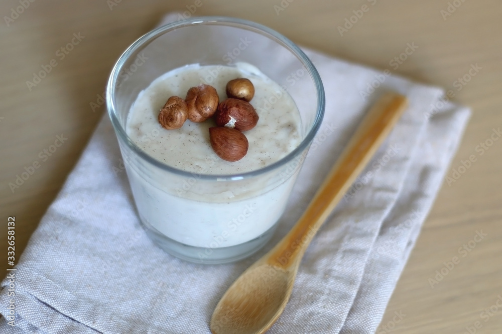 Fototapeta premium Glass of vanilla pudding with hazelnut topping and wooden spoon. Selective focus.