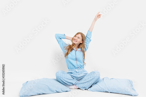 Beautiful girl in pajamas, sitting on the bed with pillows in her hands, on a white background