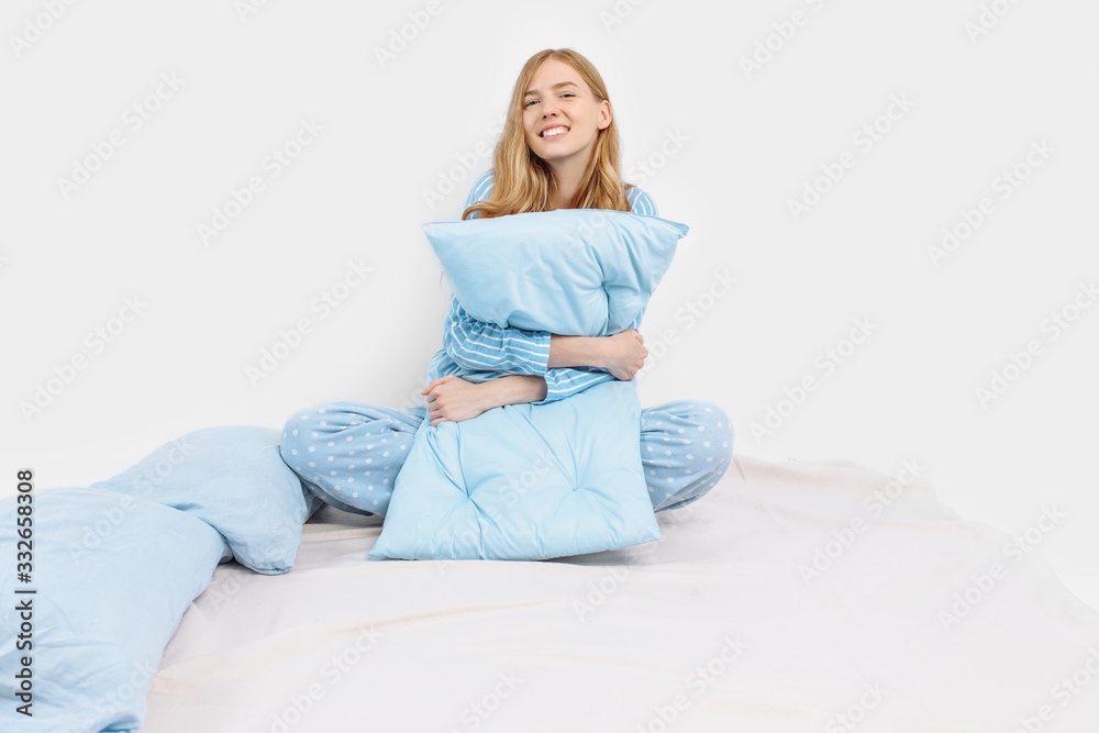 Beautiful girl in pajamas, sitting on the bed with pillows in her hands, on a white background Beautiful girl in pajamas, sitting on the bed with pillows in her hands, on a white background