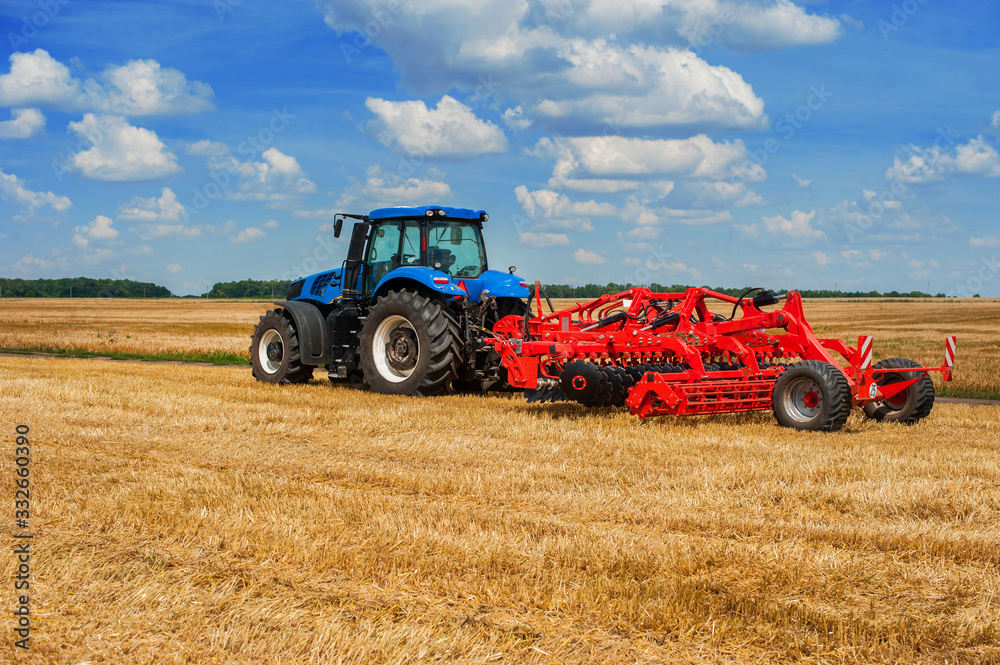 Obraz premium Farmer blue tractor working in a field, agricultural machinery in the work, tractor in the background cloudy sky
