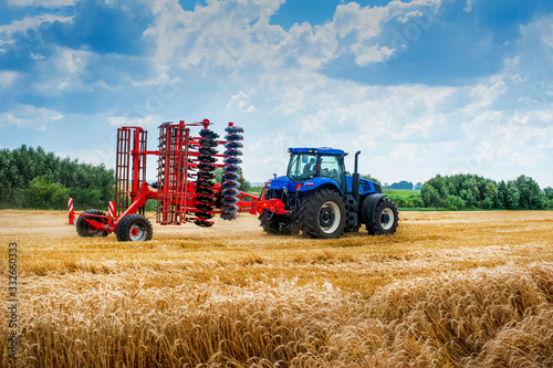 Fotografia, Obraz blue tractor pulls red harrow folded for transportation, arable land preparation