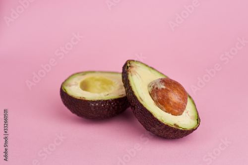 Two halves of brown mature avocado on pink background