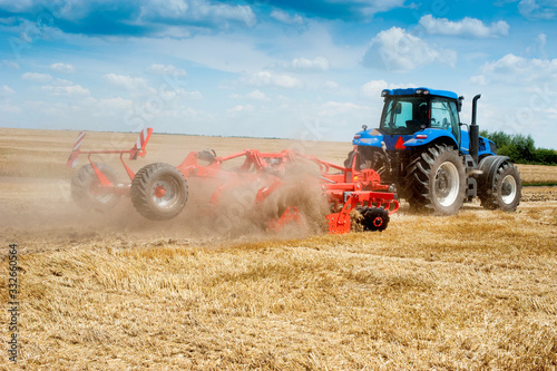 blue new tractor with red harrow in the field against a cloudy sky, agricultu...