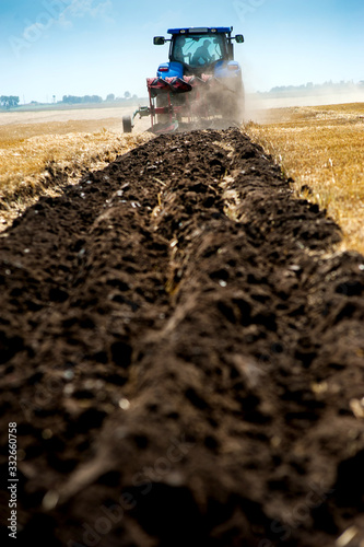 Fototapeta blue tractor pulls plow, tillage closeup in focus, agrarian preparing field