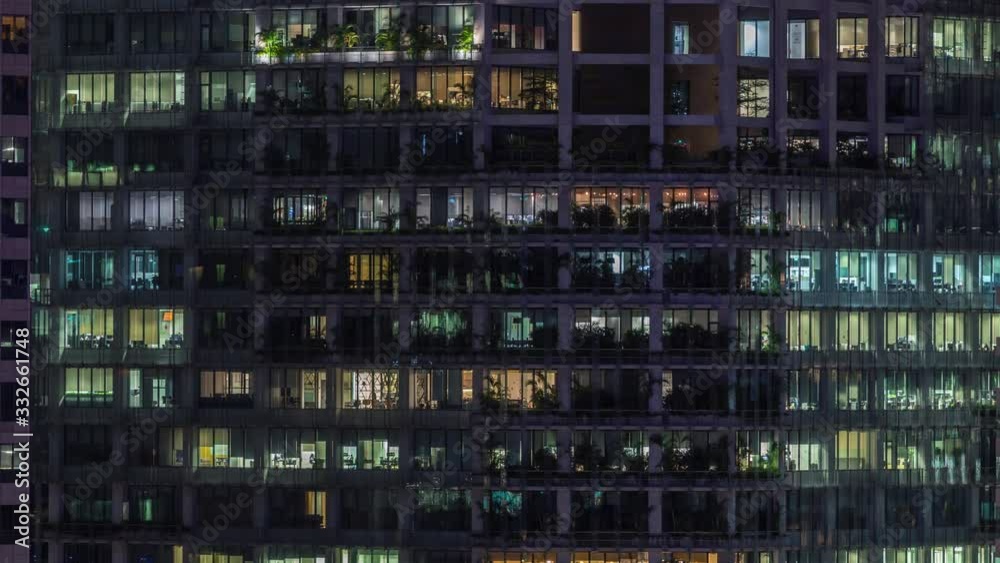 Modern office building with big windows at night timelapse close up view, in windows glowing light shines and some people inside, Singapore. Tilt up Modern office building with big windows at night timelapse close up view, in windows glowing light shines and some people inside, Singapore. Tilt up