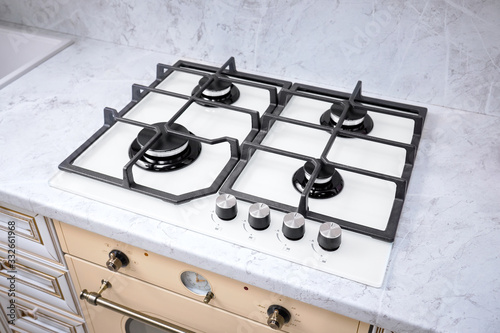 Modern hob gas stove made of tempered white glass using natural gas or propane for cooking products on light countertop in kitchen interior.