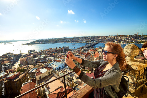 A beautiful girl tourist taking photo on her smartphone and enjoying the view of historical center of Istanbul from the top of the Galata Tower