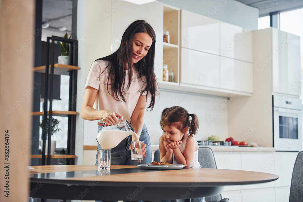Obraz premium Mother pouring fresh milk into the glass for her little daughter in kitchen