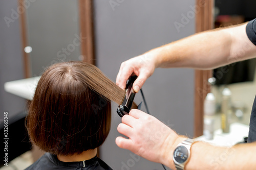 Hairdresser straightens hair of woman.