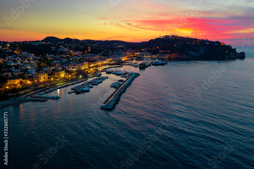 Aerial drone photo of boat docked in harbour in the island of Ischia, Italy with sunset coloured sky