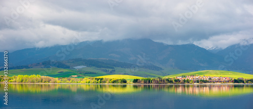lake in mountains. cloudy day in springtime. rural fields on rolling hills. beautiful scenery of high tatra mountains in dappled light. gorgeous landscape of liptovska mara, slovakia photo