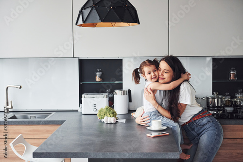 Obraz na plátne Mother with her little daughter embracing each other indoors in kitchen