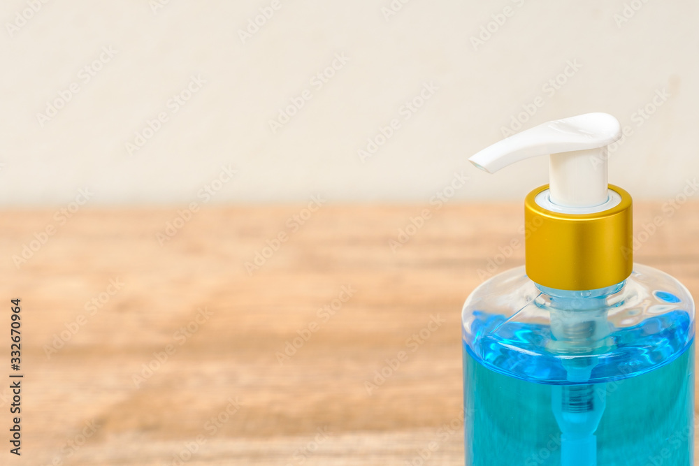 Alcohol gel in a pump bottle placed on a wooden floor beside a white wall.