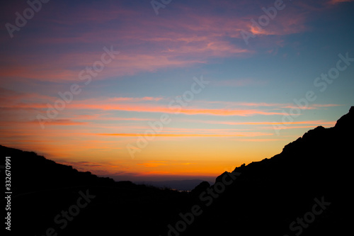 Bright pink-orange sunset sky on a black silhouette of mountains