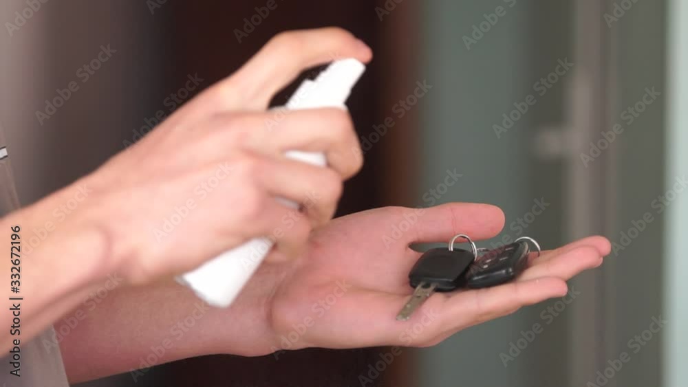 A young man disinfects car keys with an alcohol based disinfectant spray. Protective measures against the coronavirus pandemic. Cleaning and disinfecting to prevent and contain the coronavirus