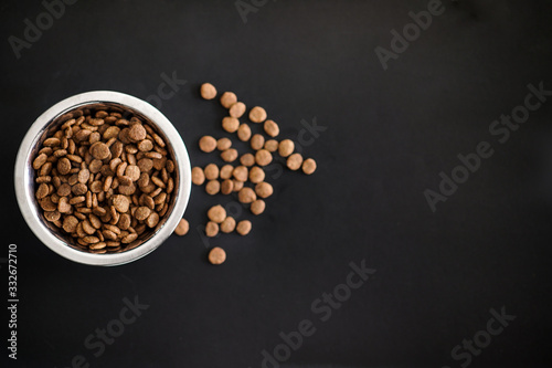 Dry cat food in a silver round dish on a black background. Flat lay, top view, copy space