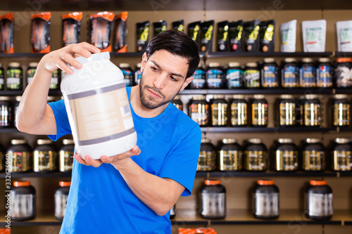 Serious young muscular man choosing sport nutrition products in shop