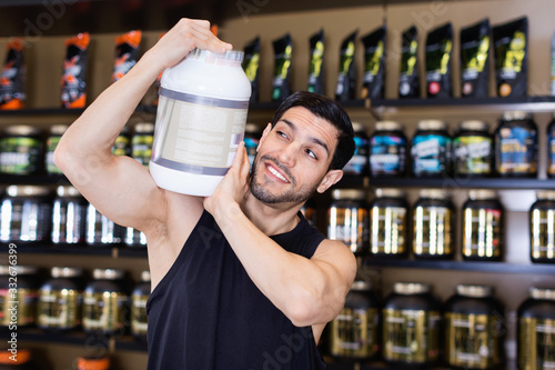 Attractive athletic man on shoulder  sport food products in store, showing his power