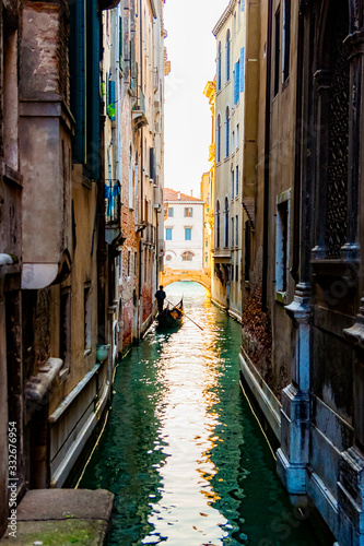 Silhouette of a lonely sad gondolier in a gondola without passengers in a narrow side channel in Venice, Italy. No people because of quarantine Covid-19 © sunday_morning