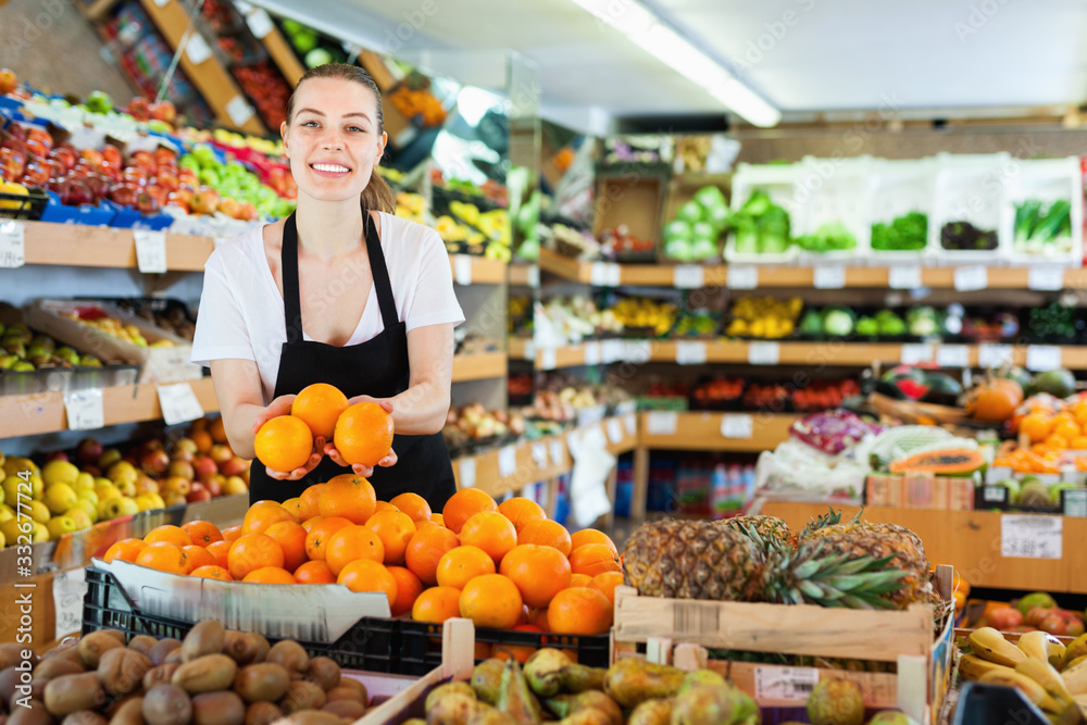 Young woman in apron working holding fresh oranges in hands on the supermarket