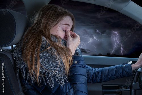 Woman driving overtired car during thunderstorm and rubbing her eyes photo