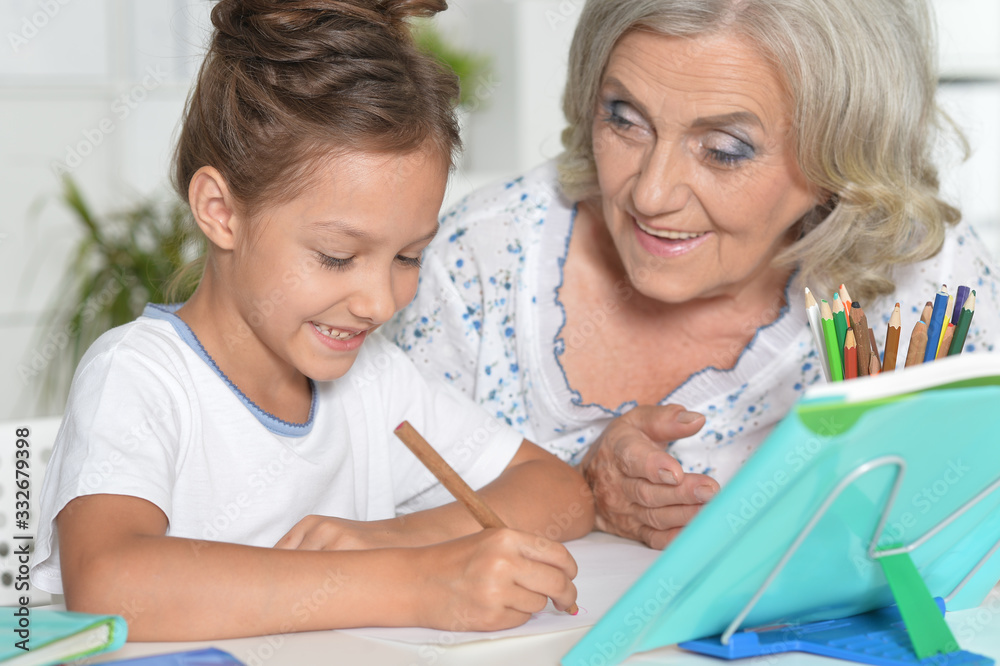 Close up portrait of grandmother with cute little girl doing homework together Close up portrait of grandmother with cute little girl doing homework together