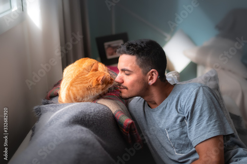 primer plano de hombre joven y gato atigrado acercandose con cariño photo