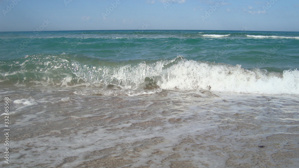 The Sea green wave runs over the smooth sandy beach, leaving a white foam on the sand. The Sea green wave runs over the smooth sandy beach, leaving a white foam on the sand.