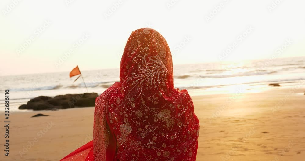 Young women wearing a red saree on the beach goa India.girl in traditional indian sari on the shore of a paradise island among the rocks and sand enjoying the freedom and the sunset