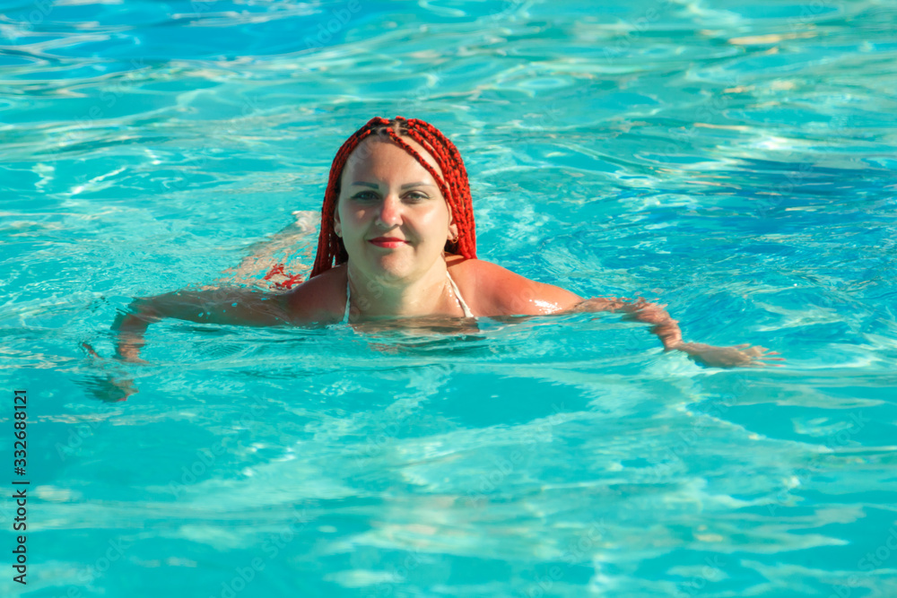 A woman with African pigtails is sitting on the edge of the pool.