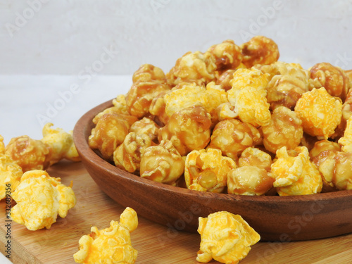 High angle view of delicious popcorn in round wooden plate isolated on wooden background. Include buttery caramel corn and rich cheddar cheese corn. Food and snack concept. With copy