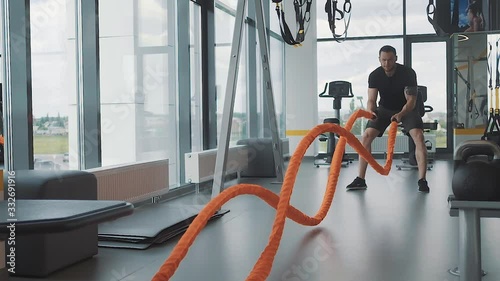 An athlete doing exercises on the rope in the gym with panoramic Windows.