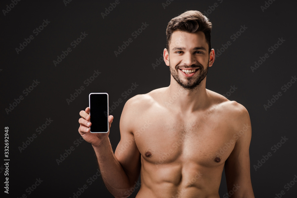 smiling sexy naked man showing smartphone with blank screen isolated on black smiling sexy naked man showing smartphone with blank screen isolated on black